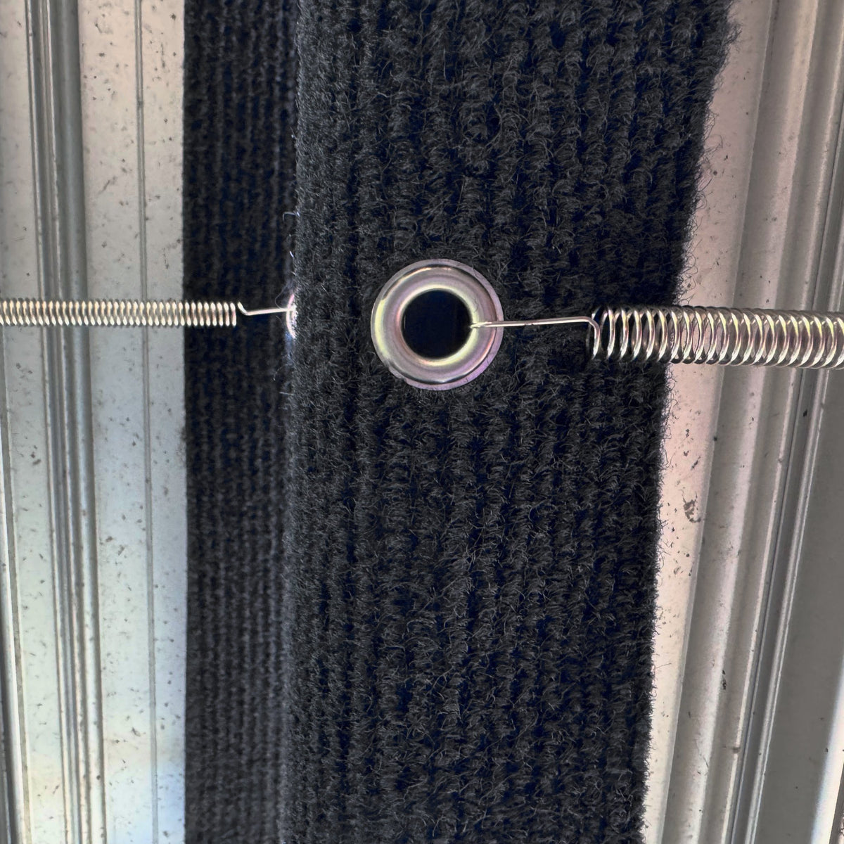 Close up of a tension spring hooked through a metal eyelet on a marine carpet step rug