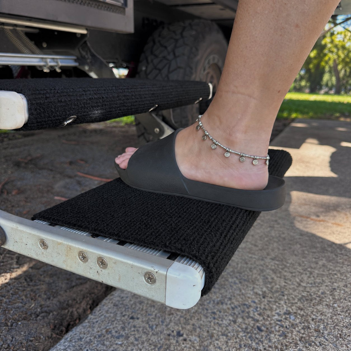 Foot in a slide stepping onto an aluminium caravan step fitted with a marine carpet rug