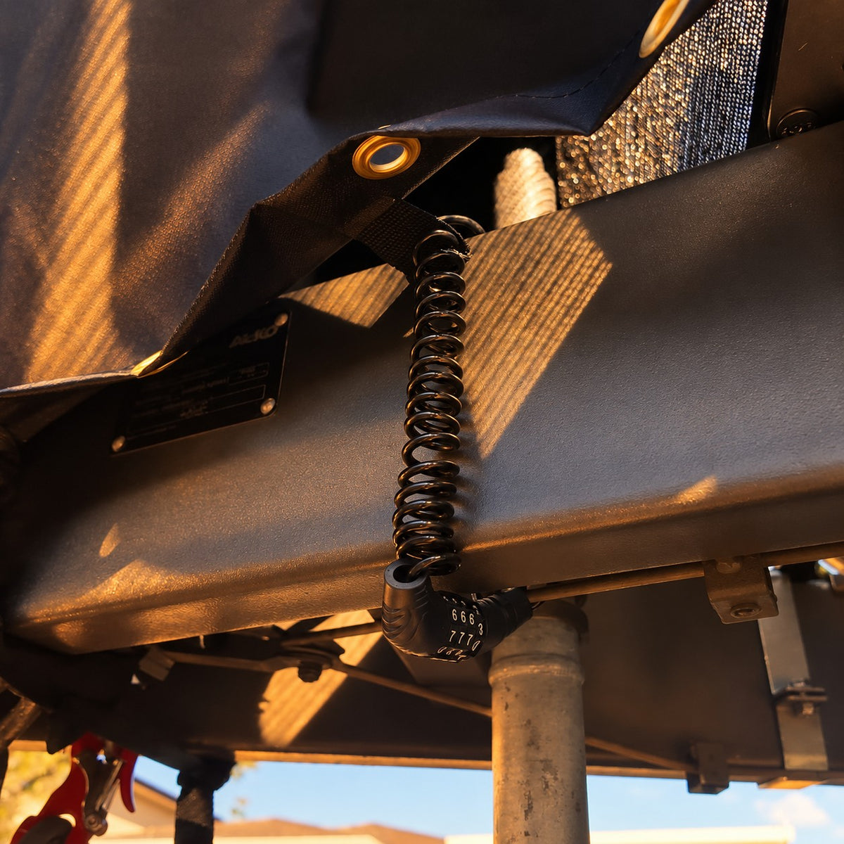 Cable lock threaded through a webbing loop under the cover and around the drawbar in warm evening light