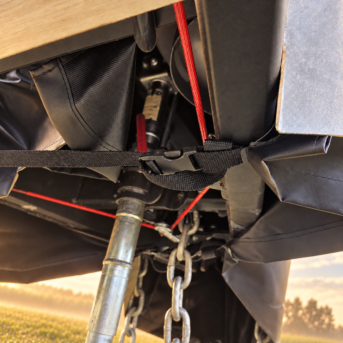 View from under the drawbar showing the open underside of the cover and a strap clipped across, with a misty paddock behind