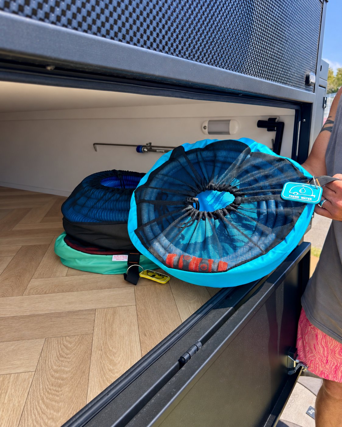 Blue drinking water hose bag being lowered into a caravan storage hatch by its handle