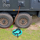 Green electrical lead bag on the grass below the caravan power inlet with an orange lead plugged in