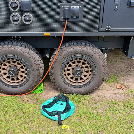 Green electrical lead bag on the grass below the caravan power inlet with an orange lead plugged in