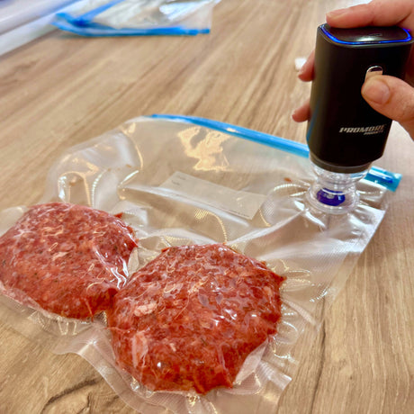 Promore portable vacuum sealer pressed onto a bag valve, drawing the bag tight around two burger patties