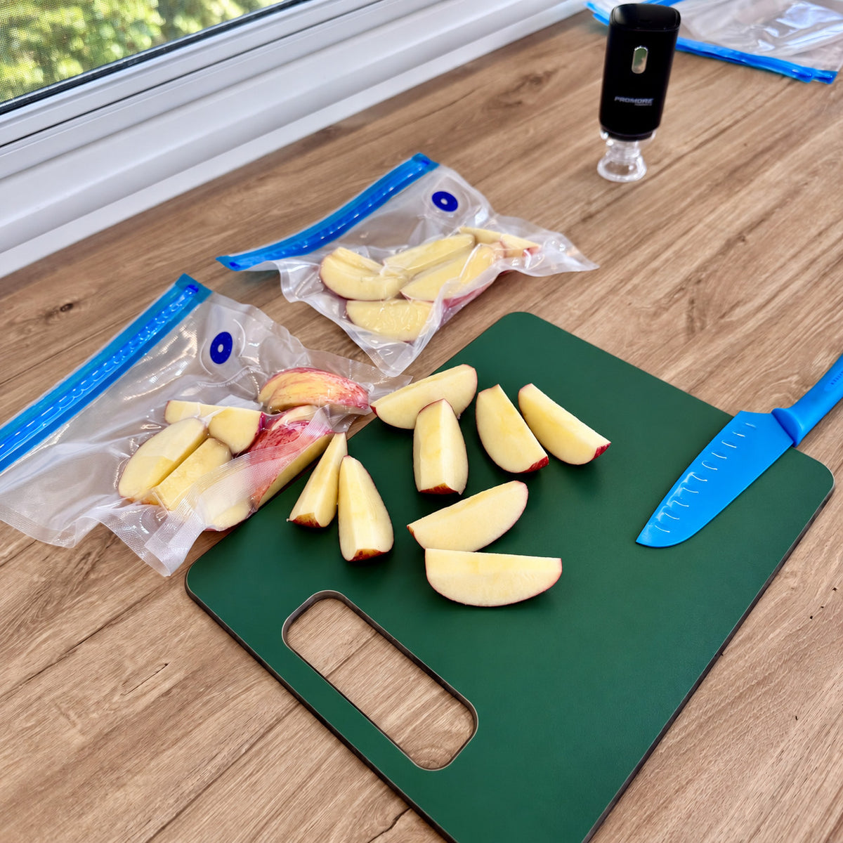 Apple slices sealed in Promore vacuum bags on a green chopping board in a caravan, with the sealer standing behind