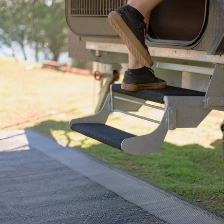 Foot stepping onto a galvanised double caravan step fitted with black marine carpet step rugs