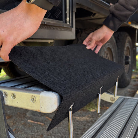 Hands laying a marine carpet step rug over the top tread of an aluminium double caravan step