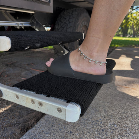 Foot in a slide stepping onto an aluminium caravan step fitted with a marine carpet rug