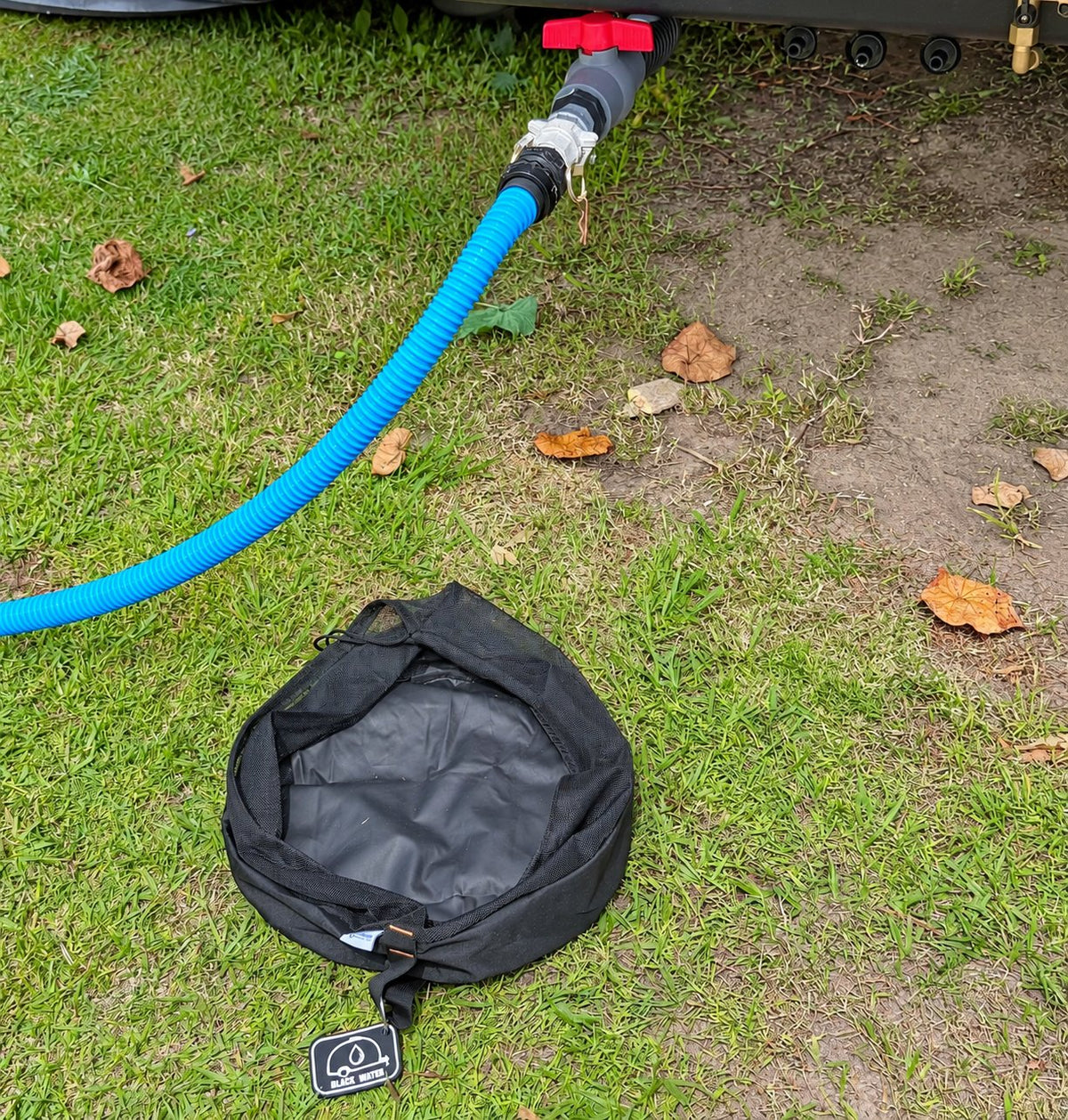 Black sullage hose bag on the grass beside the caravan waste outlet with the sullage hose connected